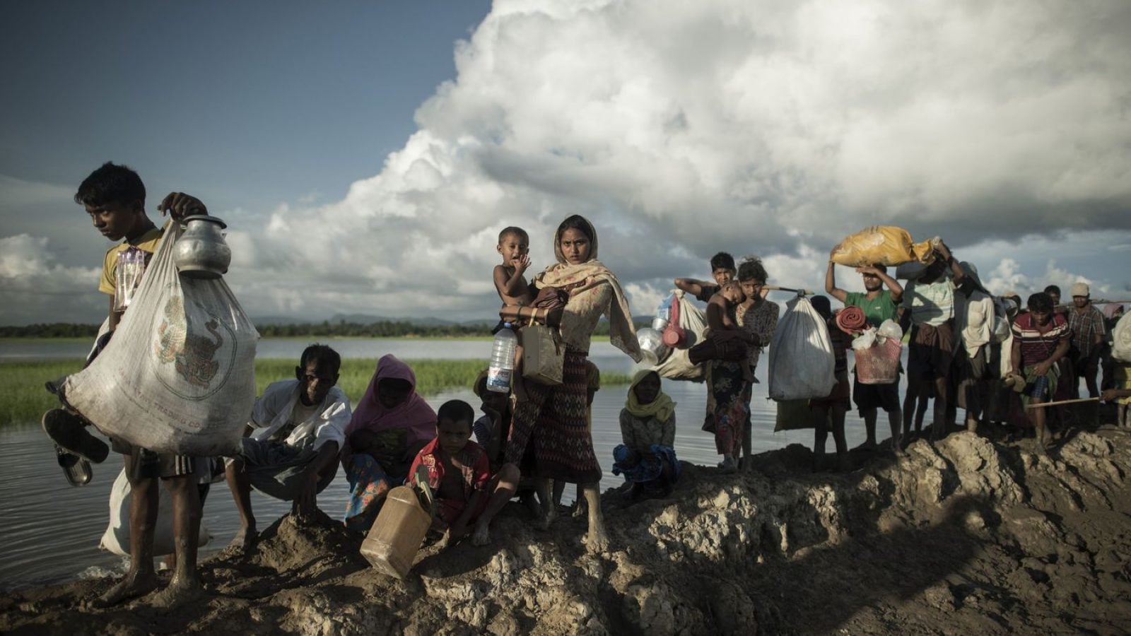 Women, children, and families walk across an earthen dam escaping ethnic persecution in Myanmar